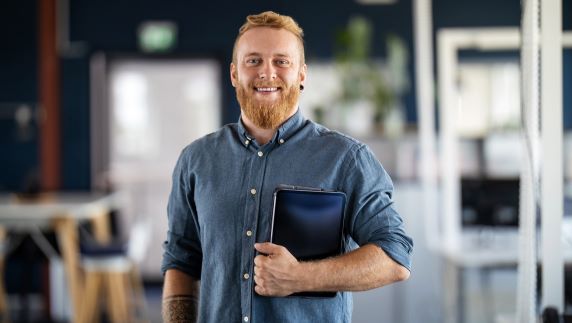 Young man smiling at camera holding tablet